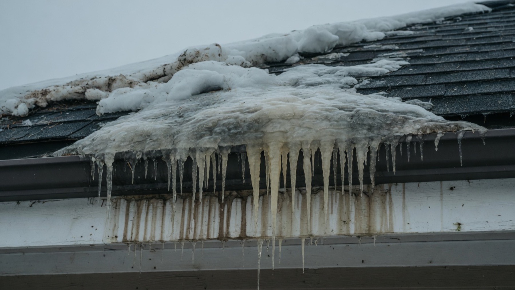 Ice dam and icicles hanging from a gutter on a winter roof in Wyoming