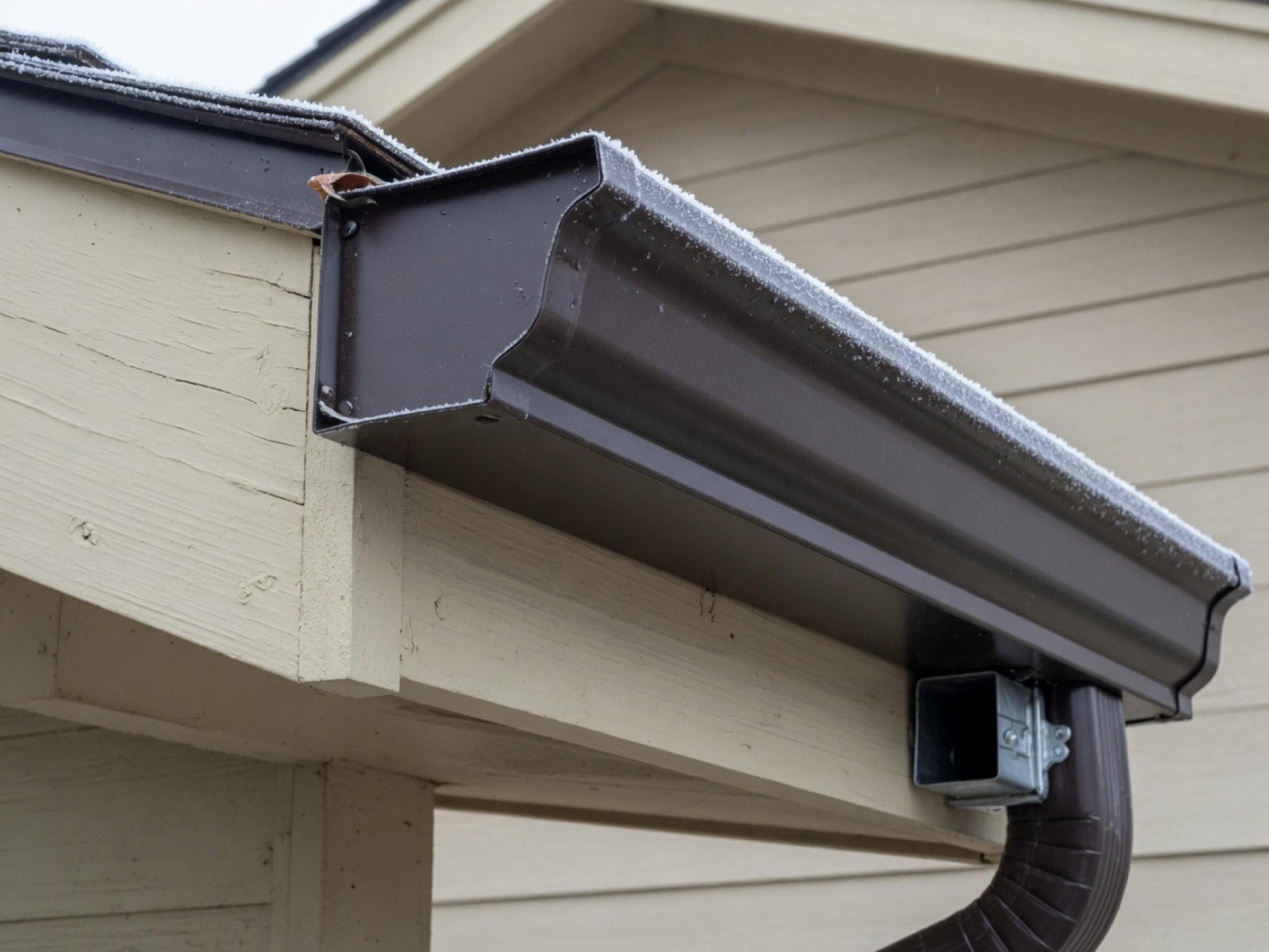Seamless dark bronze K-style aluminum gutter on a beige ranch-house fascia
